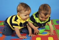 two toddler boys crawling on a colorful play mat