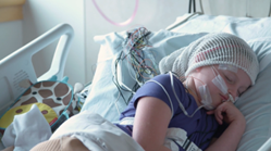 A child with wires attached to her head and body rests in hospital bed while undergoing a sleep study.