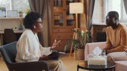 An African American man speaking with a female psychologist during a therapy session.