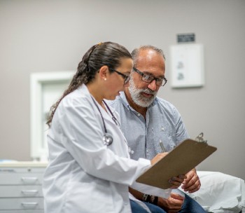 A health care provider sits next to an older adult patient reviewing the patient chart together