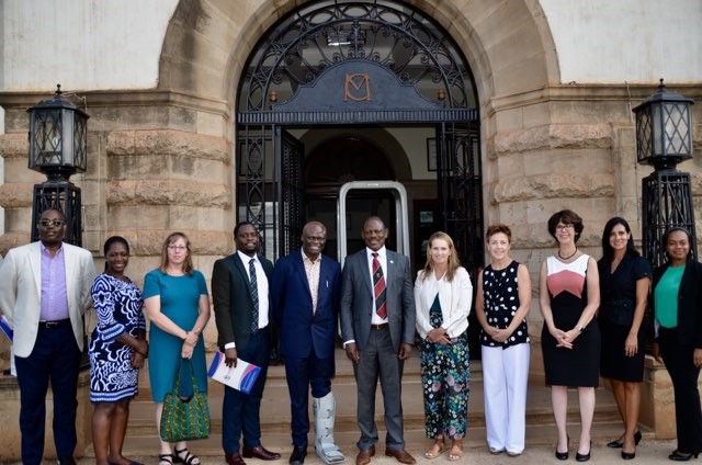 A group of 11 NIMH staff and researchers from Washington University stand in front of a building on the Makerere University  Campus. 