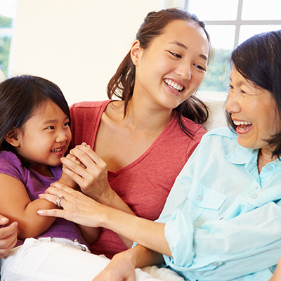 Grandmother laughing with granddaughter and daughter on sofa