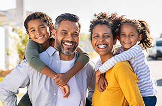 photo of a family of four, a man holds a young boy on his back and a woman holds a young girl on her back