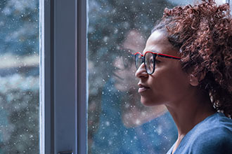 A woman staring out the window while it’s snowing