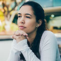 a teen girl sits with her elbows propped, resting her chin on her folded hands.