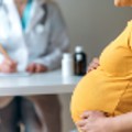 Pregnant woman holds her baby bump while a therapist in the background takes notes. 