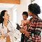 Infant and female caregiver holding tablet and speaking with doctor.