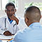 a male doctor faces the camera, listening to a male patient facing away from the camera