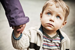 young boy looking up, holding adults hand