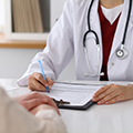 Close up of a female doctor’s hands filling out a screening form while speaking with a patient