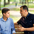 A father and son sitting on a park bench.