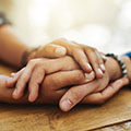 Photo of a pair of woman’s hands holding another woman’s hand on a table.